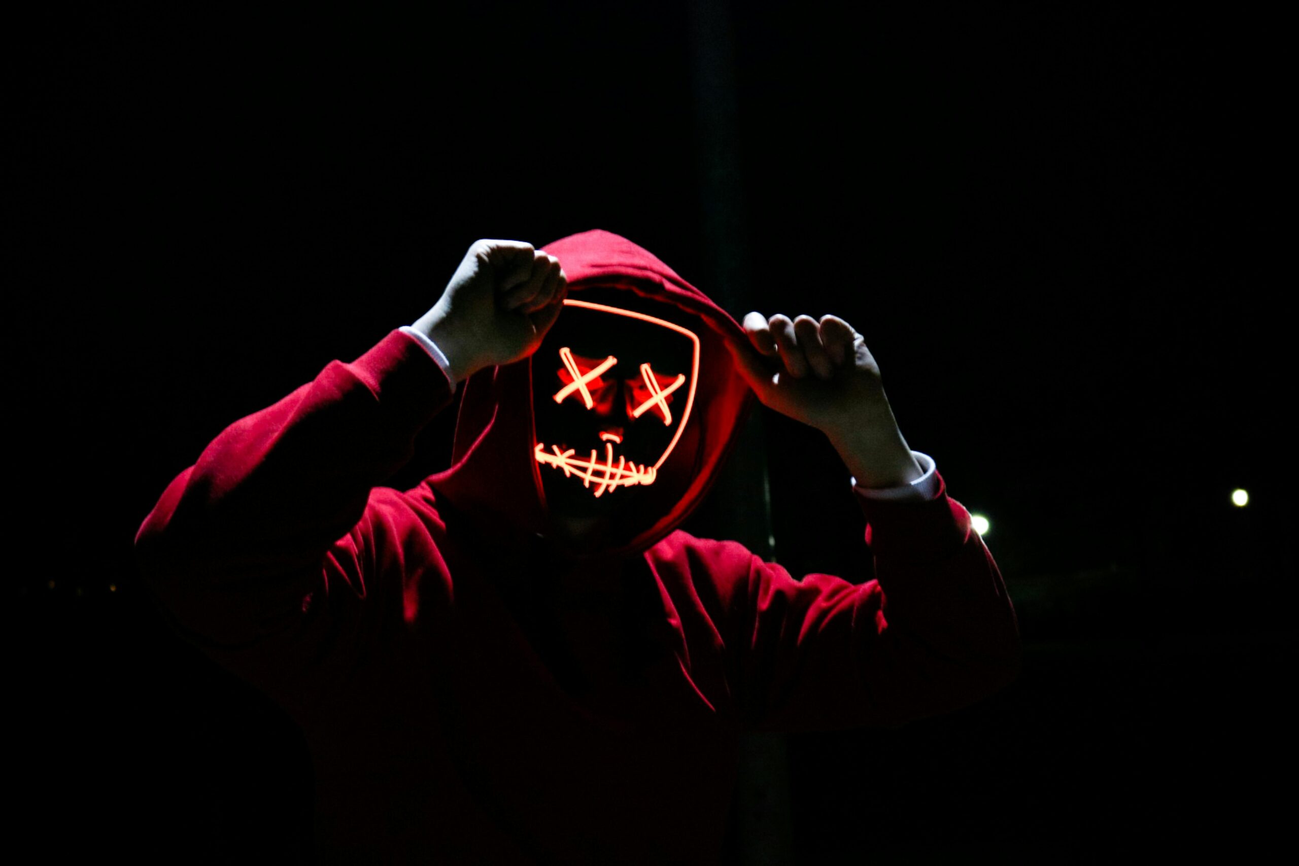 pexels-photo-1097456-1097456 A spooky illuminated mask figure with a red hoodie in a dark setting, perfect for Halloween themes.